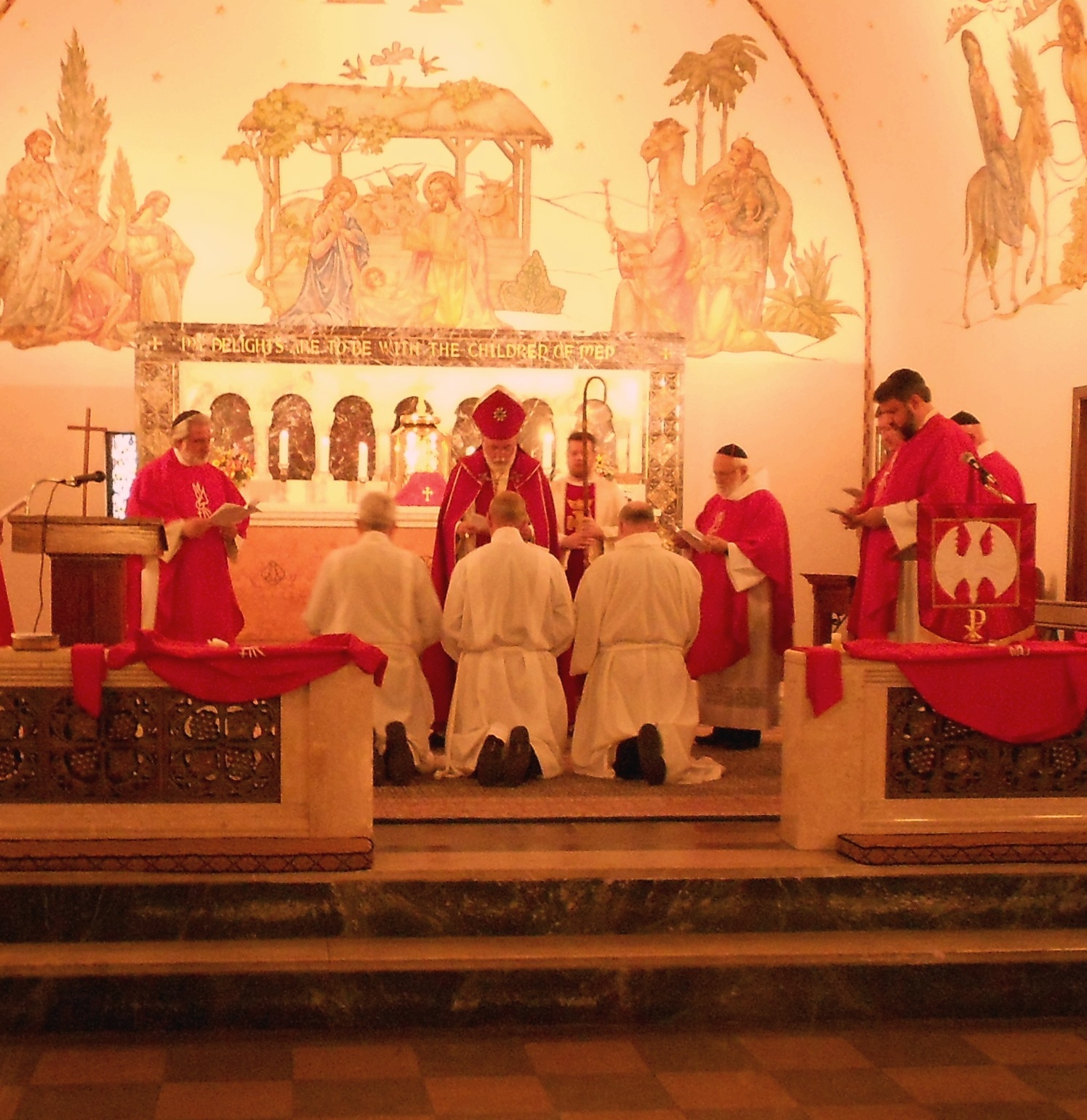 Ordination service at the altar, with clergy in red vestments and candidates kneeling